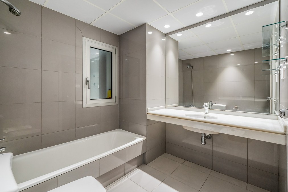 Baño en tonos grises con bañera, ventana y espejo grande